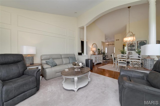 living area with ornate columns, wood finished floors, a chandelier, arched walkways, and high vaulted ceiling