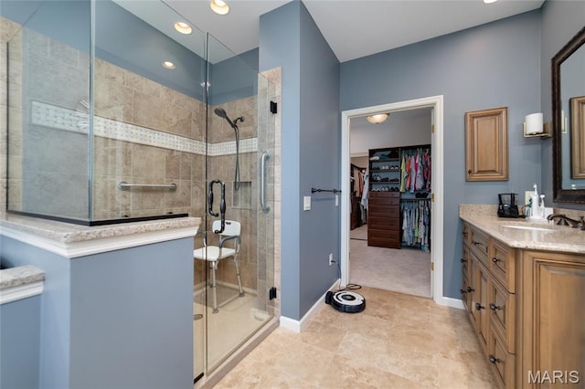 bathroom with a stall shower, vanity, a spacious closet, baseboards, and recessed lighting