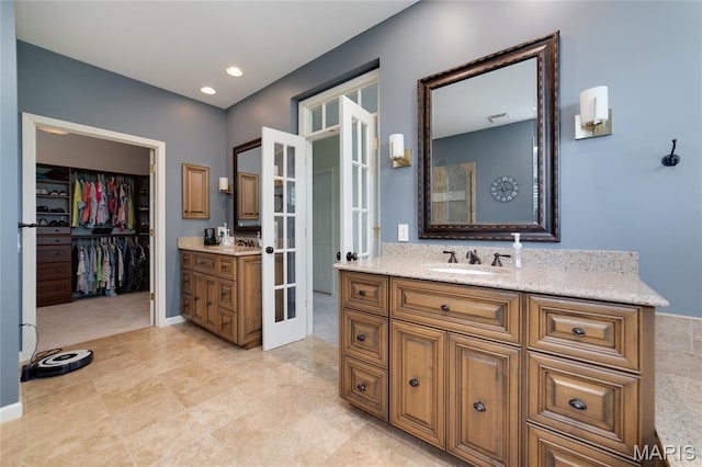 bathroom featuring french doors, vanity, a walk in closet, and recessed lighting