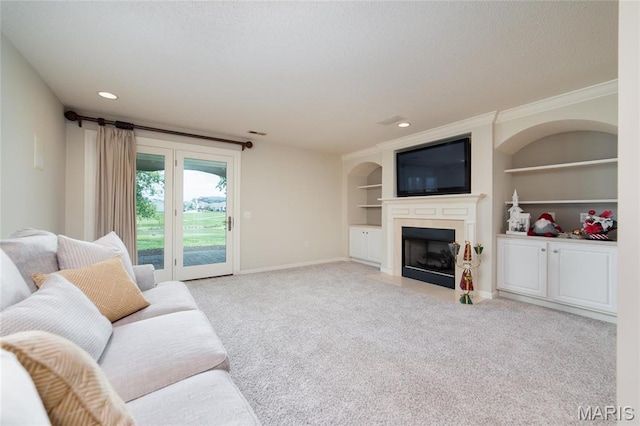 living room with a fireplace with flush hearth, built in features, crown molding, light colored carpet, and baseboards