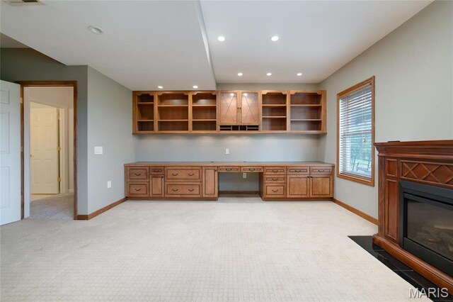 unfurnished office with light carpet, built in desk, baseboards, recessed lighting, and a fireplace with flush hearth