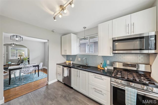 5909 Hampton Ave, Saint Louis, MO 63109 - kitchen featuring appliances with stainless steel finishes, a sink, dark countertops, white cabinetry, and tasteful backsplash