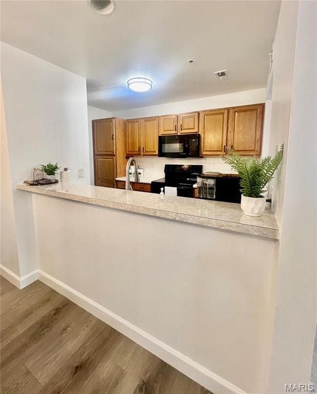 3605 Tracey Rich Rd Unit 1A, Saint Louis, MO 63125 - kitchen with black appliances, wood finished floors, a peninsula, baseboards, and decorative backsplash