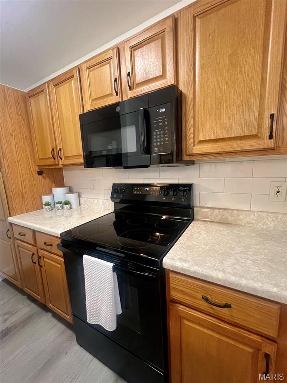 3605 Tracey Rich Rd Unit 1A, Saint Louis, MO 63125 - kitchen with black appliances, light wood-style floors, light countertops, and decorative backsplash