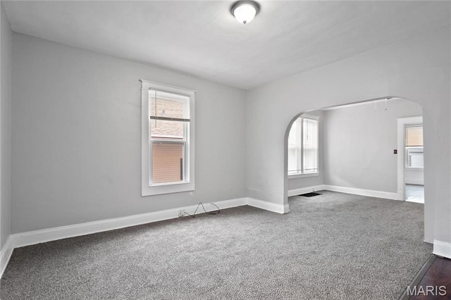 carpeted spare room with arched walkways and baseboards