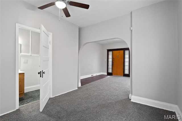 spare room with arched walkways, dark carpet, a ceiling fan, and baseboards