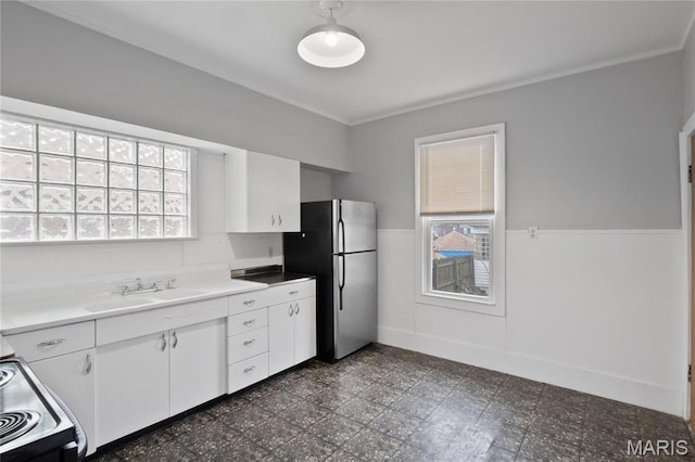 kitchen featuring freestanding refrigerator, a wainscoted wall, white cabinets, crown molding, and dark floors