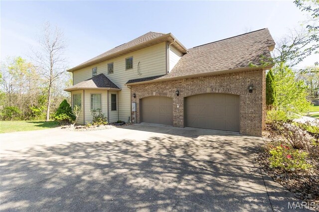 traditional home with driveway, a garage, brick siding, and a shingled roof