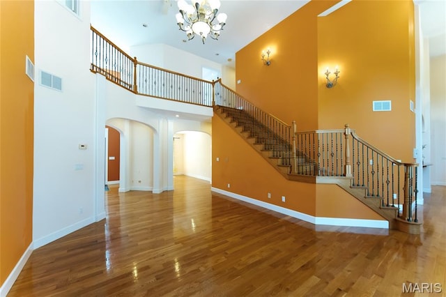 1025 Cobblestone Dr, Rolla, MO 65401 - unfurnished living room featuring arched walkways, a towering ceiling, a chandelier, wood finished floors, and stairs