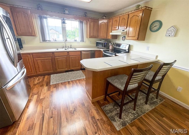 11652 Two Mile Rd, Dexter, MO 63841 - kitchen with stainless steel appliances, under cabinet range hood, a peninsula, wood finished floors, and ornamental molding