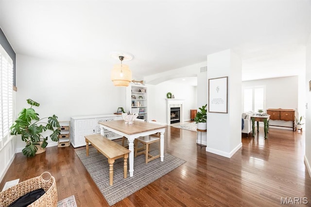 dining room featuring a fireplace with flush hearth, wood finished floors, baseboards, and arched walkways