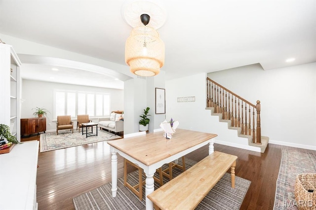 dining space with arched walkways, wood finished floors, baseboards, recessed lighting, and stairs