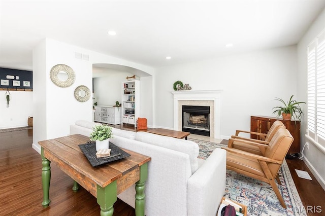 living room with wood finished floors, arched walkways, plenty of natural light, a fireplace with flush hearth, and recessed lighting