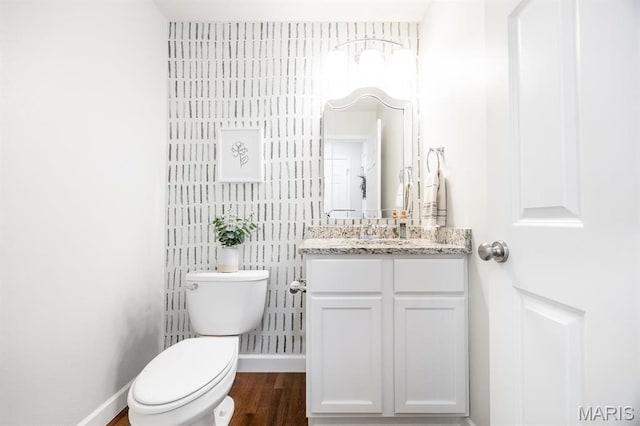 half bathroom with baseboards, toilet, wood finished floors, and vanity
