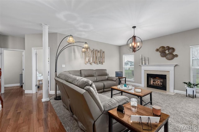 living area with a chandelier, decorative columns, a fireplace, baseboards, and dark wood-type flooring