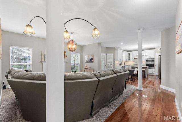 living room featuring decorative columns, hardwood / wood-style flooring, and baseboards