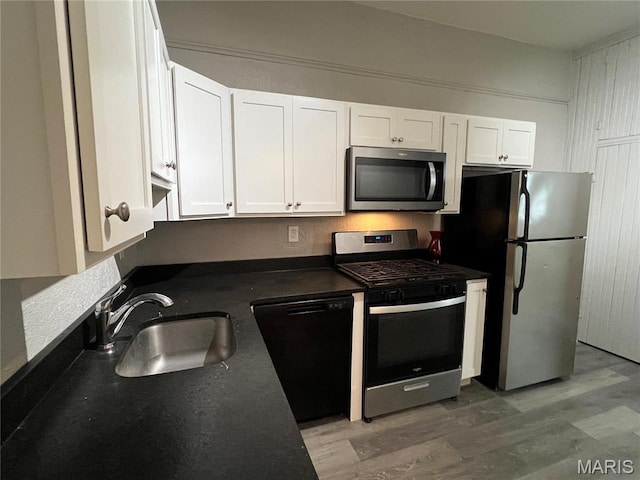 8423 Tennessee Ave, Saint Louis, MO 63125 - kitchen with appliances with stainless steel finishes, a sink, dark countertops, white cabinets, and wood finished floors
