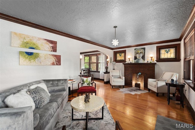 living area featuring arched walkways, wood finished floors, ornamental molding, a textured ceiling, and baseboards