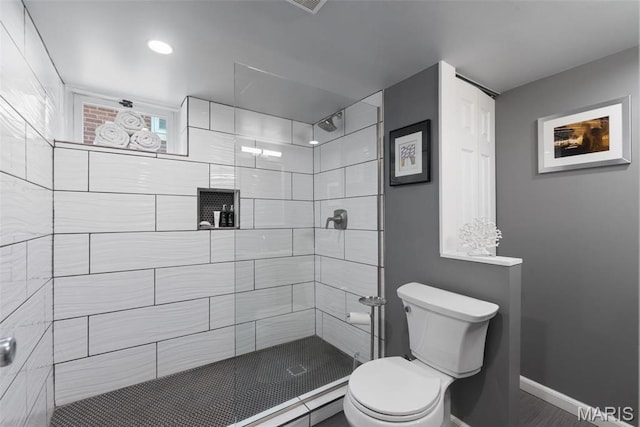 full bathroom with toilet, a tile shower, and baseboards