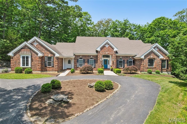 view of front of property featuring curved driveway, a front lawn, and roof with shingles