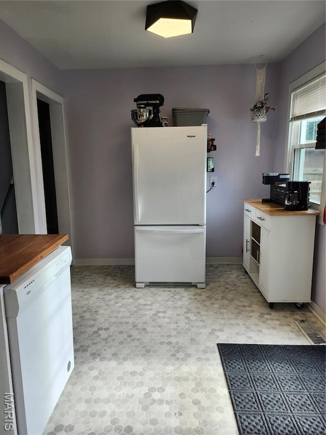 kitchen with white appliances, butcher block counters, baseboards, and white cabinets