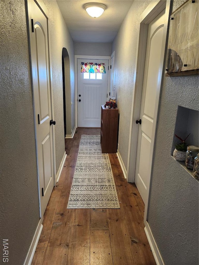 entryway with arched walkways, hardwood / wood-style flooring, a textured wall, and baseboards