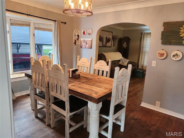 dining space featuring arched walkways, a chandelier, hardwood / wood-style flooring, and baseboards