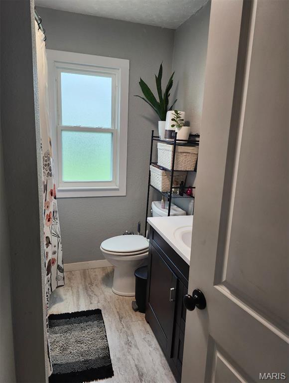 bathroom featuring vanity, toilet, wood finished floors, baseboards, and a shower with shower curtain
