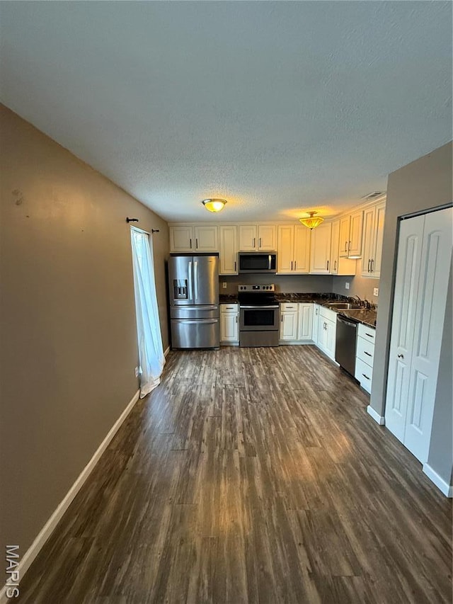 kitchen featuring appliances with stainless steel finishes, dark countertops, dark wood finished floors, baseboards, and a textured ceiling