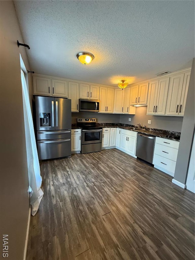 kitchen featuring stainless steel appliances, dark countertops, a textured ceiling, dark wood finished floors, and a sink