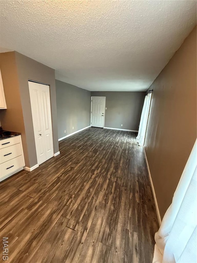 unfurnished living room with dark wood-type flooring, baseboards, and a textured ceiling