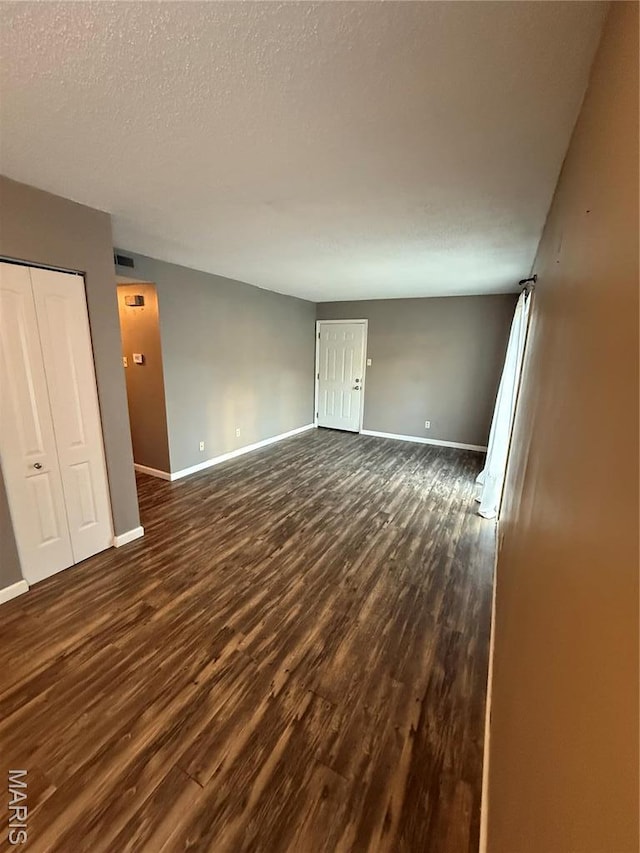 unfurnished room featuring baseboards, dark wood-style floors, and a textured ceiling