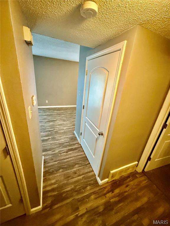 corridor featuring wood finished floors, baseboards, and a textured ceiling