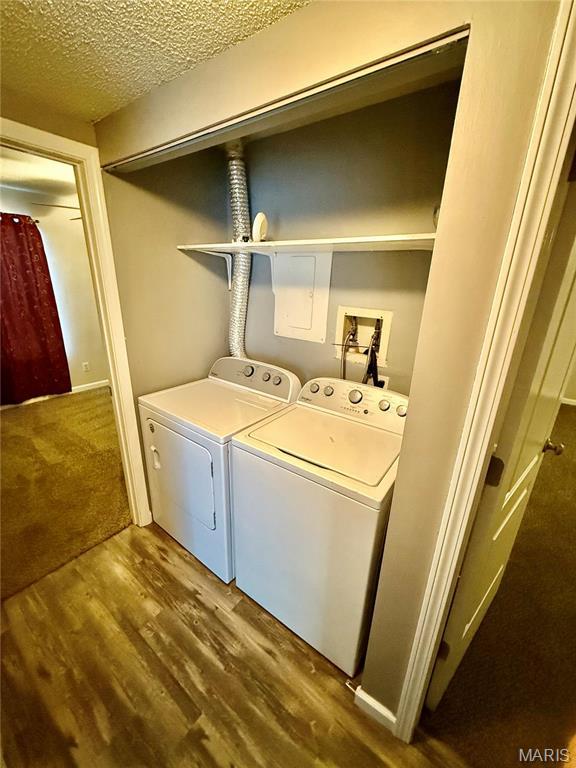 clothes washing area with washing machine and dryer, wood finished floors, and a textured ceiling