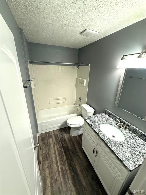 bathroom with a textured ceiling, wood finished floors, vanity, toilet, and tub / shower combination
