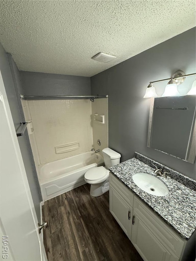 bathroom featuring wood finished floors, toilet, a textured ceiling, vanity, and bathtub / shower combination