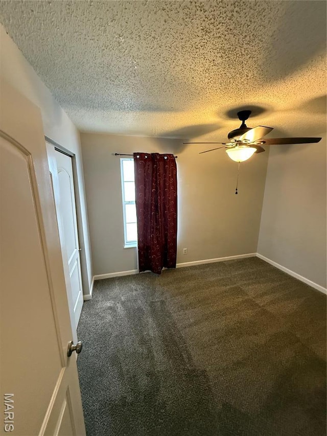 unfurnished room featuring a textured ceiling, a ceiling fan, dark colored carpet, and baseboards