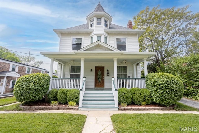 view of front of property with a chimney, a ceiling fan, a porch, and a front lawn