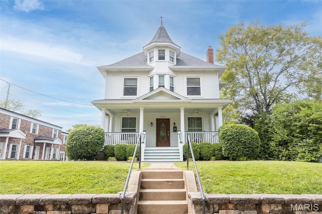 victorian home featuring a chimney, a porch, a front yard, and roof with shingles