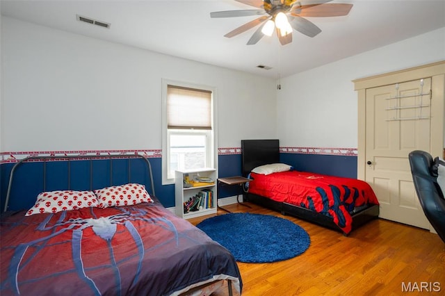 bedroom with wood finished floors, wainscoting, and a ceiling fan