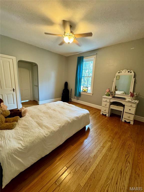 149 N Elizabeth Ave, Saint Louis, MO 63135 - bedroom with wood finished floors, arched walkways, baseboards, a textured ceiling, and a ceiling fan