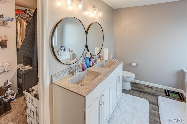 bathroom with wood finished floors, vanity, a walk in closet, baseboards, and toilet