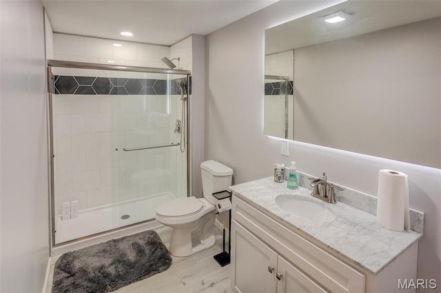 bathroom with a shower stall, toilet, vanity, and wood finished floors