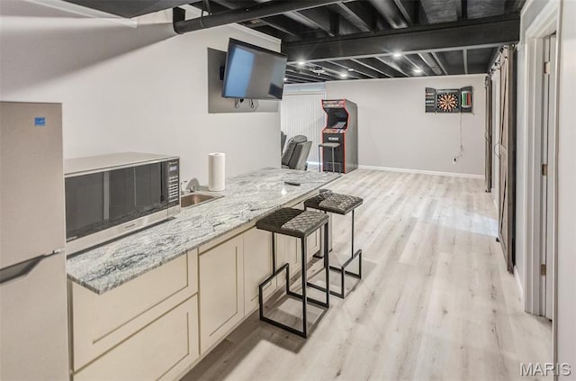 kitchen featuring freestanding refrigerator, stainless steel microwave, light wood-style floors, cream cabinetry, and light stone counters