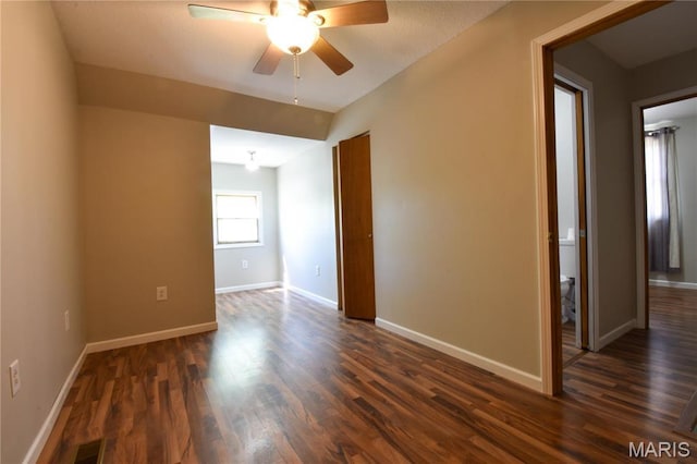empty room featuring dark wood-style flooring, a ceiling fan, and baseboards