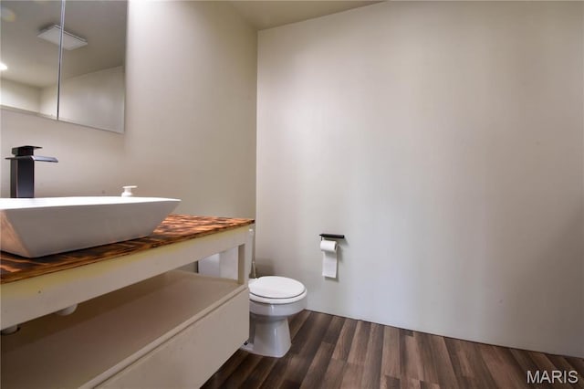 half bath with toilet, wood finished floors, and vanity