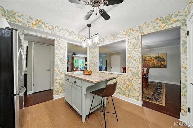kitchen with freestanding refrigerator, wallpapered walls, a ceiling fan, baseboards, and a breakfast bar area