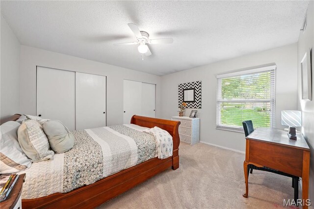 bedroom with two closets, light colored carpet, ceiling fan, a desk, and baseboards