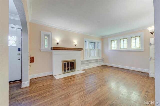 unfurnished living room featuring ornamental molding, wood finished floors, a brick fireplace, and baseboards
