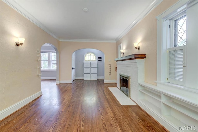 unfurnished living room featuring arched walkways, ornamental molding, wood finished floors, baseboards, and a fireplace